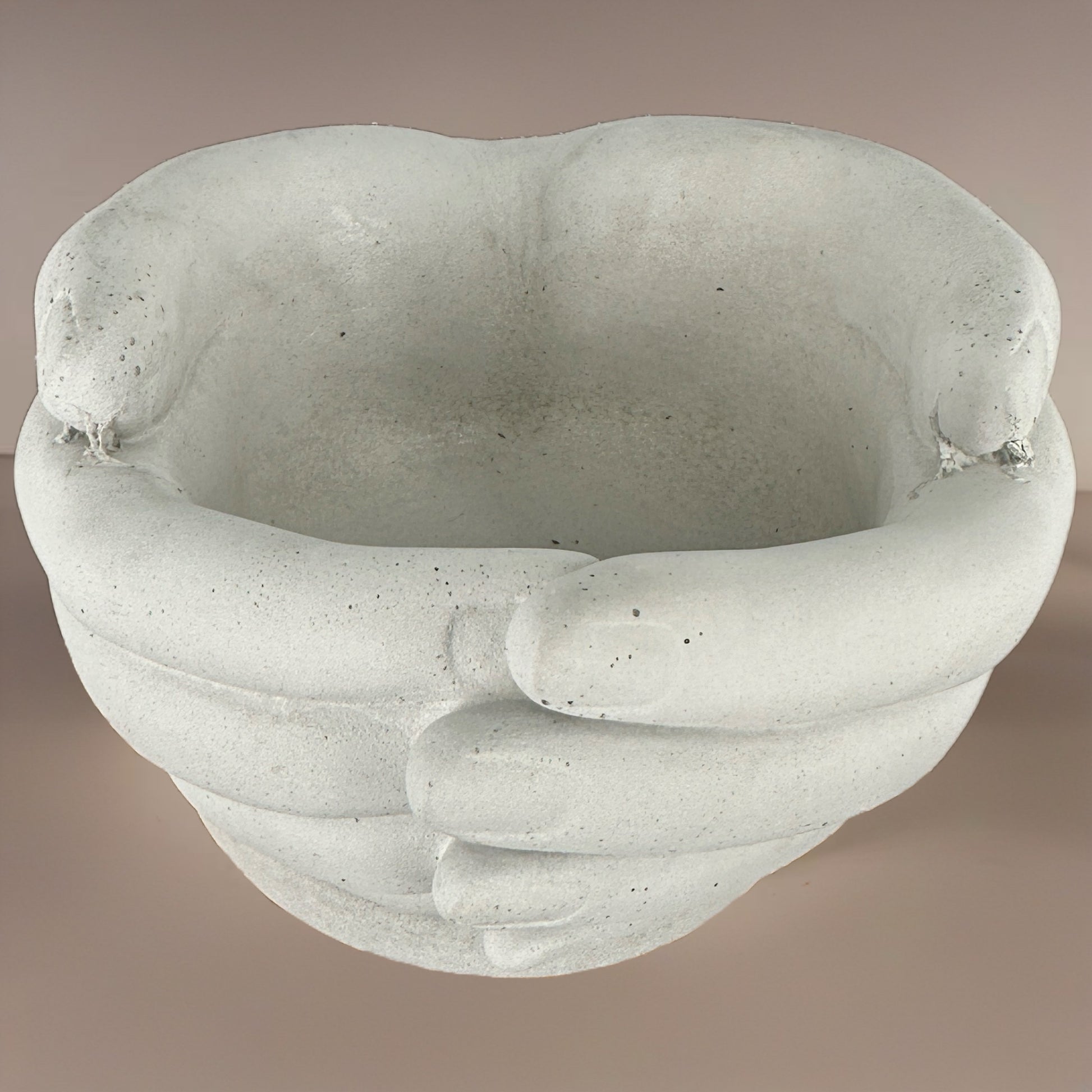 Overhead view of a sculpted concrete planter designed as interlocked hands forming a circular opening