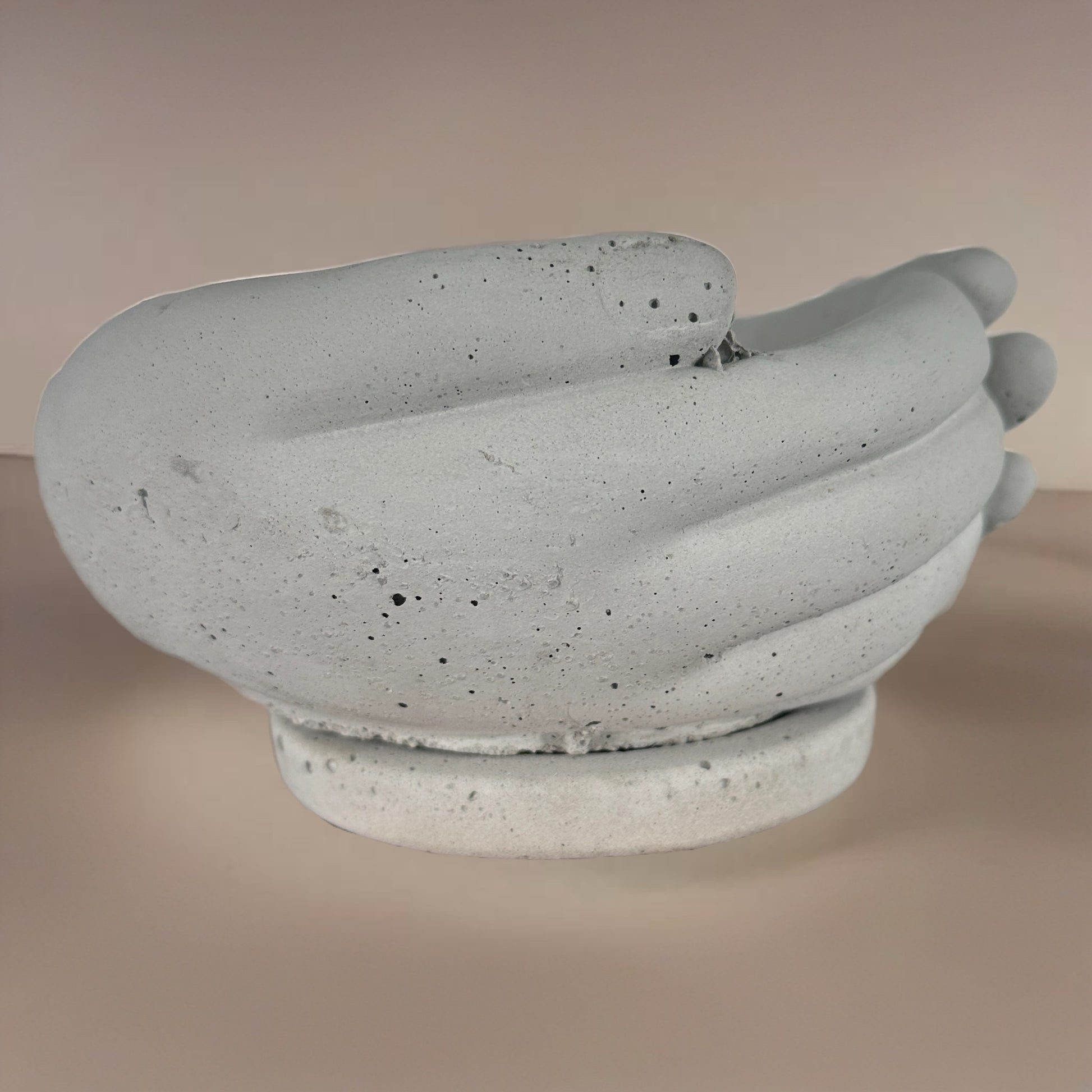 Side profile of a concrete planter sculpted as clasped hands, highlighting the texture and curvature of the design